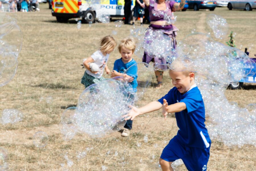 a boy wearing a blue football kit chasing bubbles with two other children in the background