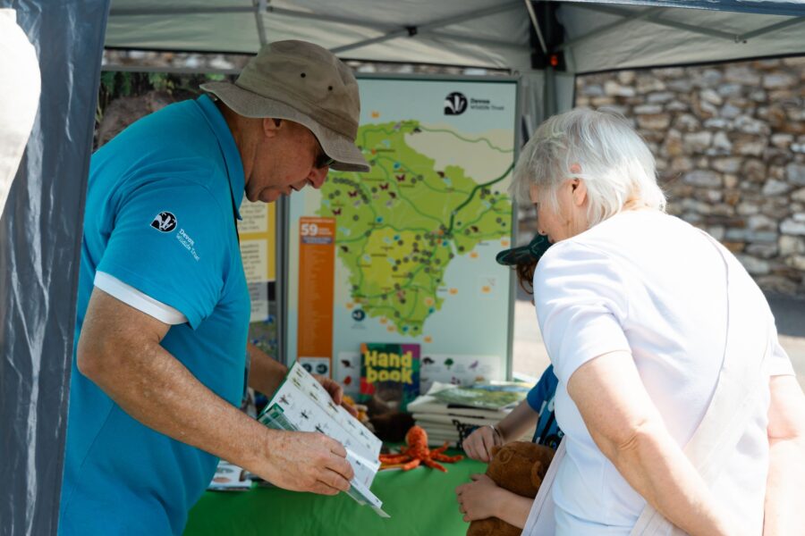 a man wearing Devon Wildlife Trust shirt at their stall on Northcote Lane showing a leaflet to two people