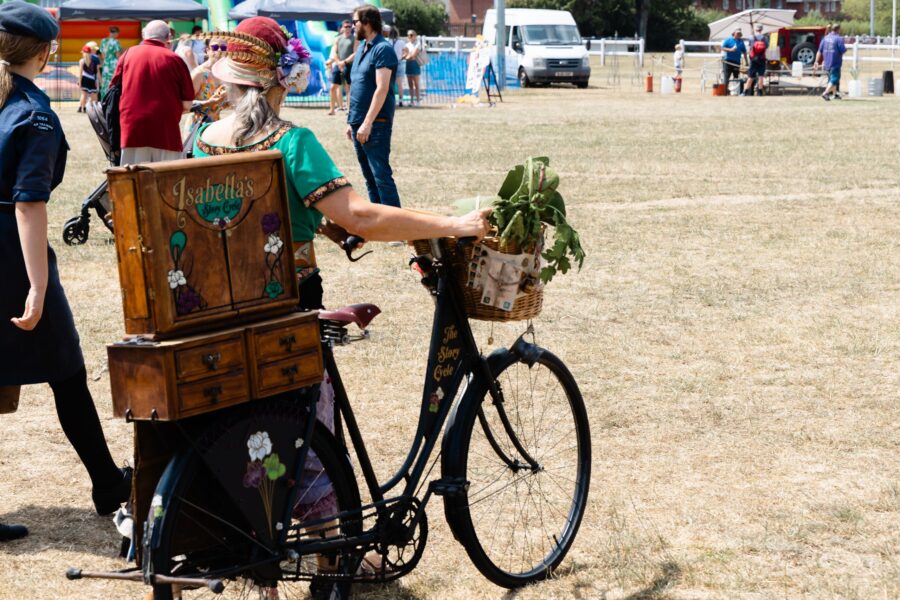 a lady pushing an old fashioned ladies bicycle with a wooden box labelled Isabella's Story Cycle