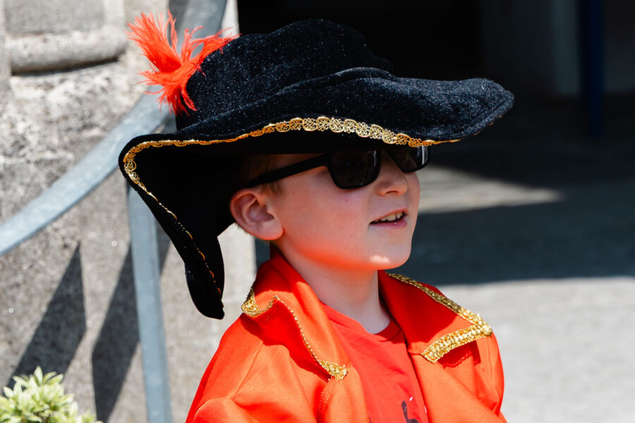 an entrant in the junior town crier competition in orange cloak and tricorn hat and carrying small handbell