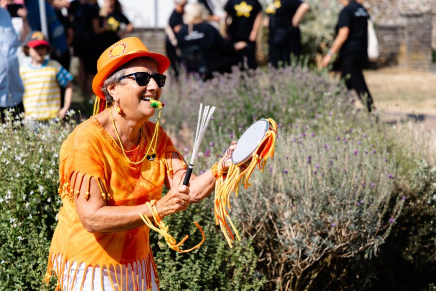 a member of Sunshine Samba playing a tambourine and blowing a whistle outside St Paul's Church