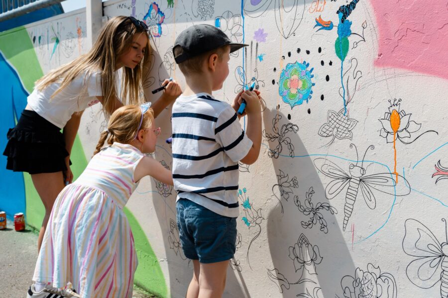 three children colouring in the doodle wall at the skate park on Allhallows field at Charet Day 2026