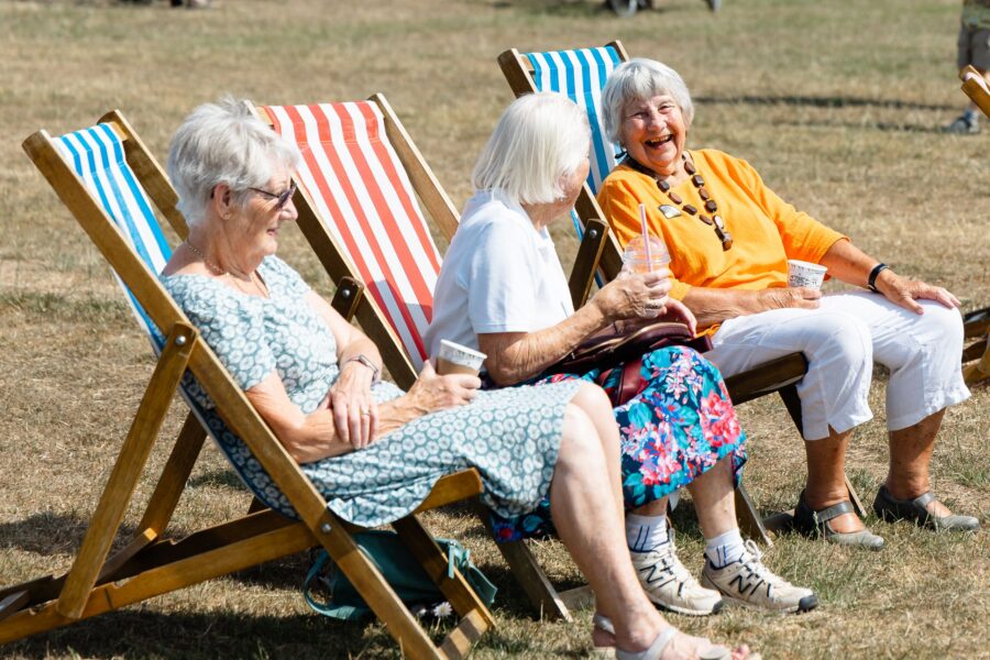three ladies sitting on striped deckchairs holding coffee cups and laughing