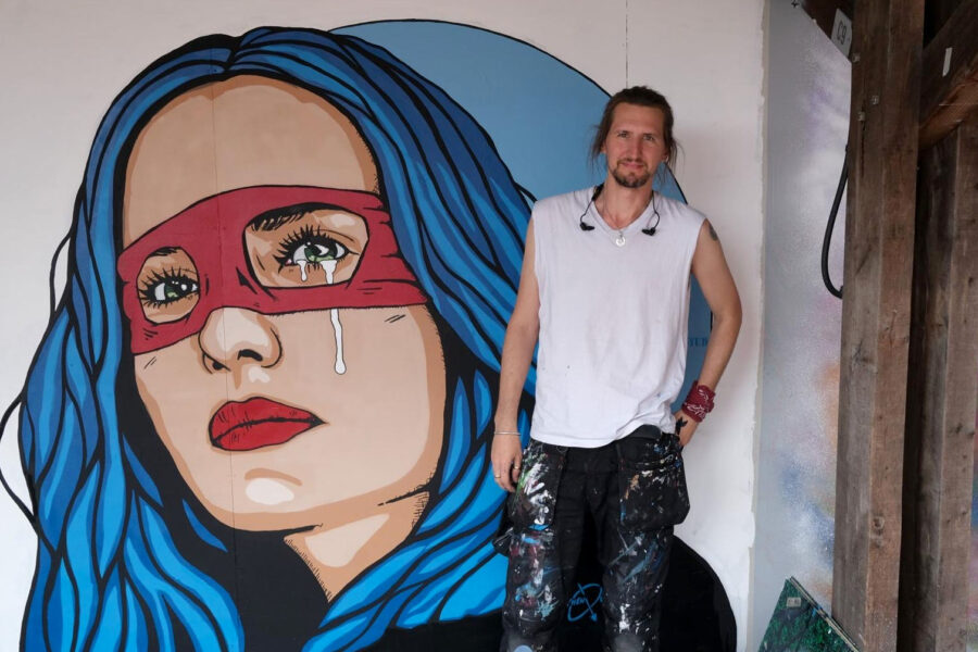 Street artist Stephen Quick standing in front of his "skater girl" mural of a young woman with bright blue hair